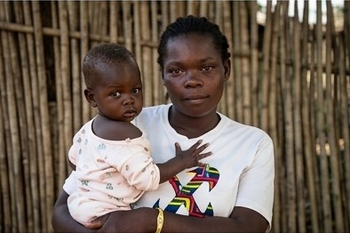 A mother holding her young child outside a home in South Sudan